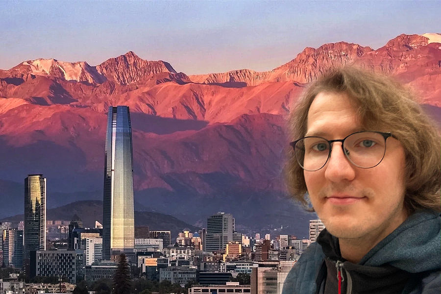 Porträt eines Mannes mit Brille vor der Skyline von Santiago mit hohen Gebäuden und Bergen im Hintergrund bei Sonnenuntergang